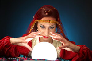 Woman in red with a veil holding her hands around a glowing crystal ball