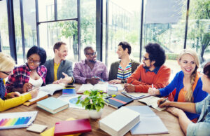 Multi-ethnic group of mixed genders wearing bright colors meeting around a table piled with books and note books
