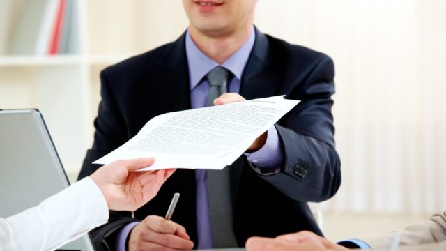 A person handing a man in a suit some documents