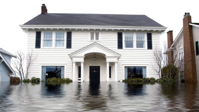 Large White two-story home with black shutters submerged in water halfway up the lower level