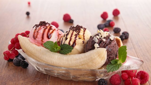 banana split with strawberry, vanilla and chocolate ice cream, a banana, chocolate sauce, sprinkle, mint and berries on a wooden table