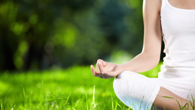 white person wearing white doing lotus pose in the green grass