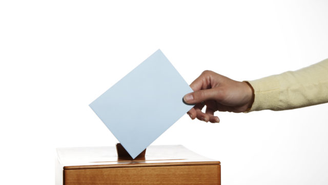 a female hand putting a ballot in a ballot box
