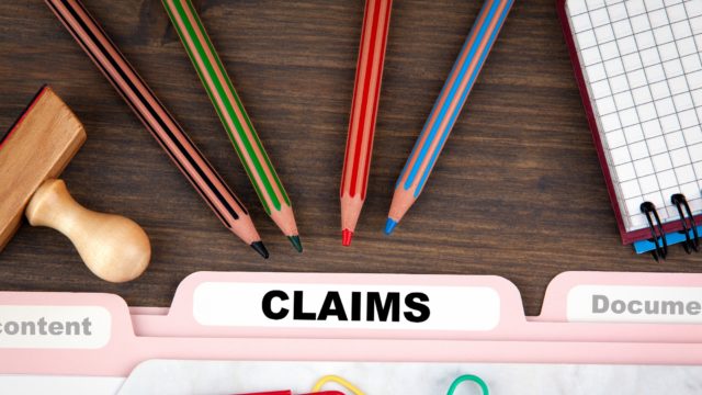 file folder with the word "claims" on it surrounded by colored pencils, paper clips, a stamp and graph paper