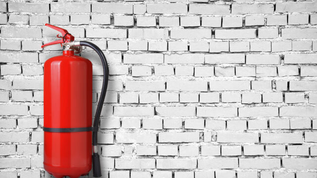 A white brick wall with a red fire extinguisher hanging on the left side of it
