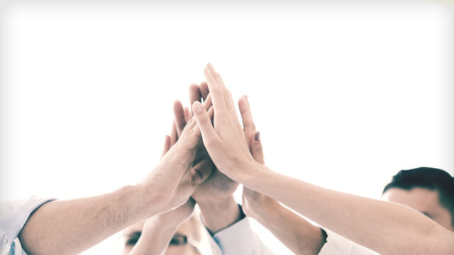 Hands coming together in the middle of a circle, some wearing business attire