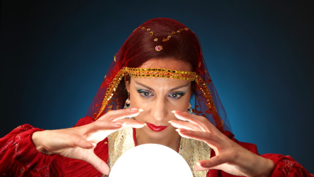 Woman in red with a veil holding her hands around a glowing crystal ball